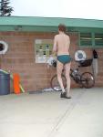 Reading the bulletin board in a green Nike speedo, black nike slippers (rear)