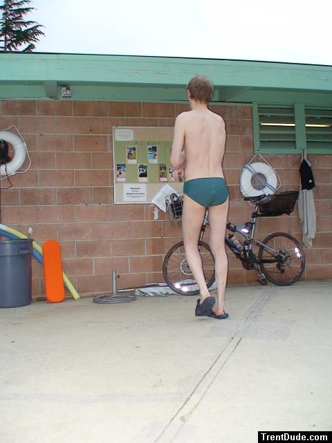 Reading the bulletin board in a green Nike speedo, black nike slippers (rear)