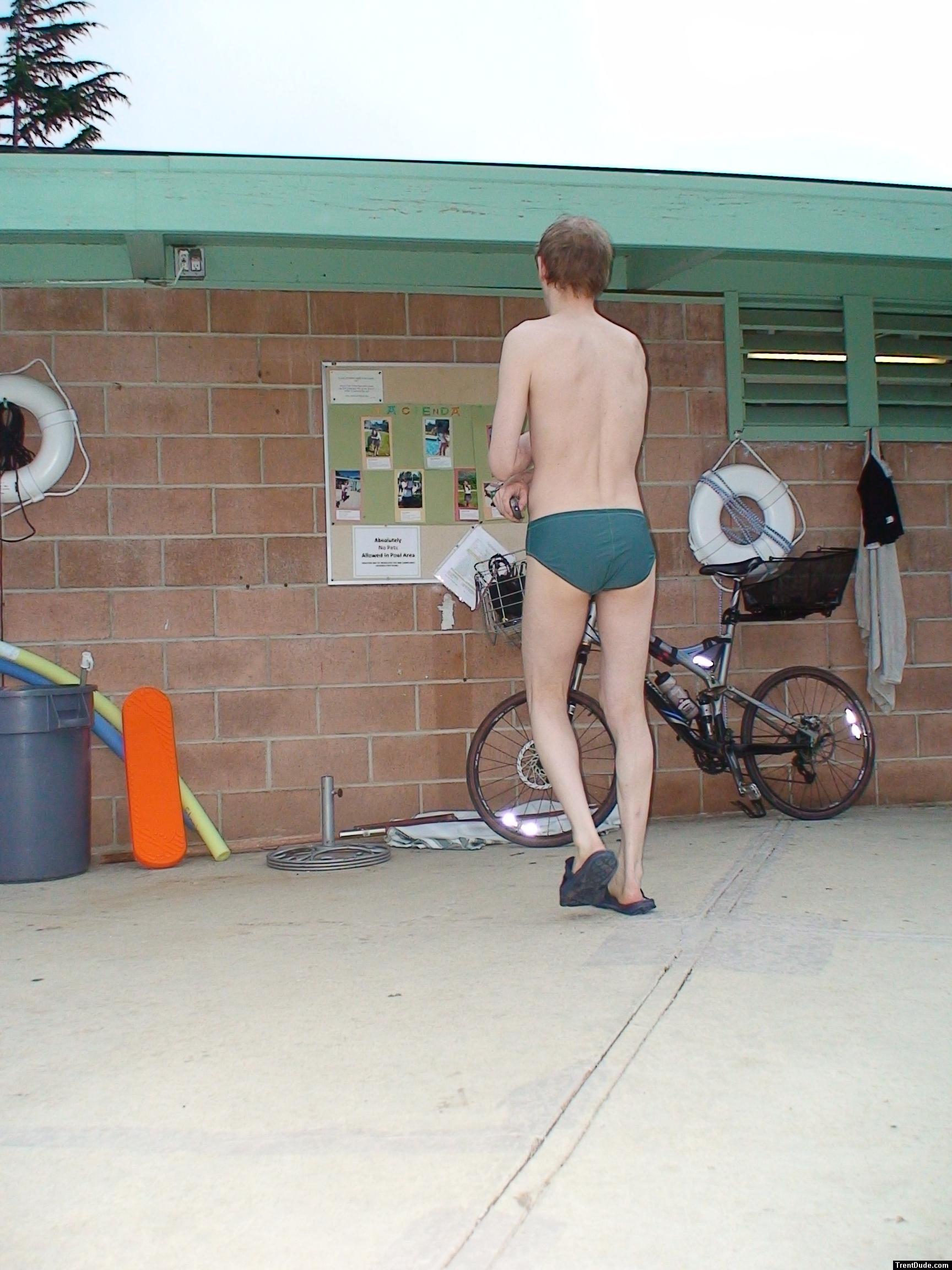 Reading the bulletin board in a green Nike speedo, black nike slippers (rear)